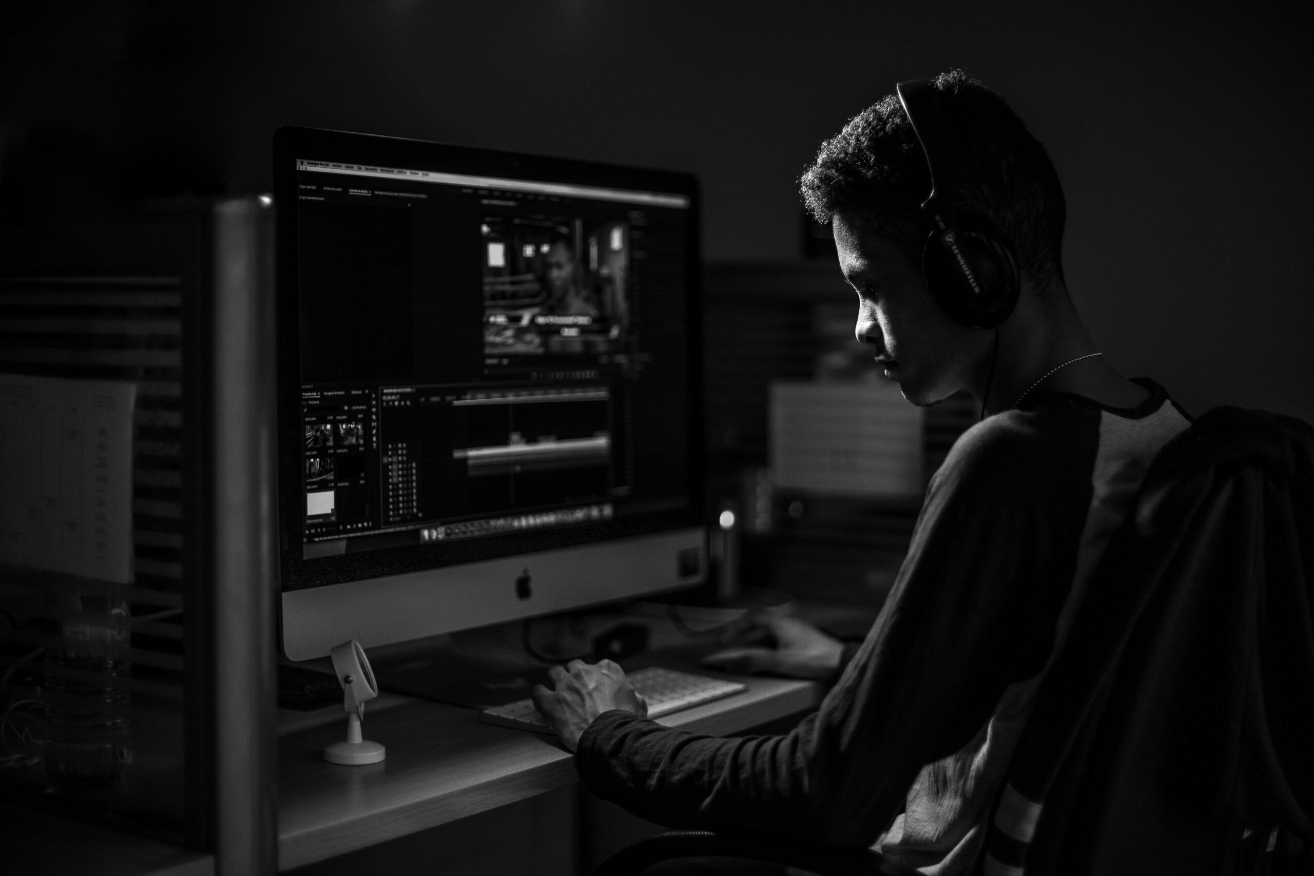 IT Services A man wearing headphones working on video editing on a computer in a dimly lit office.