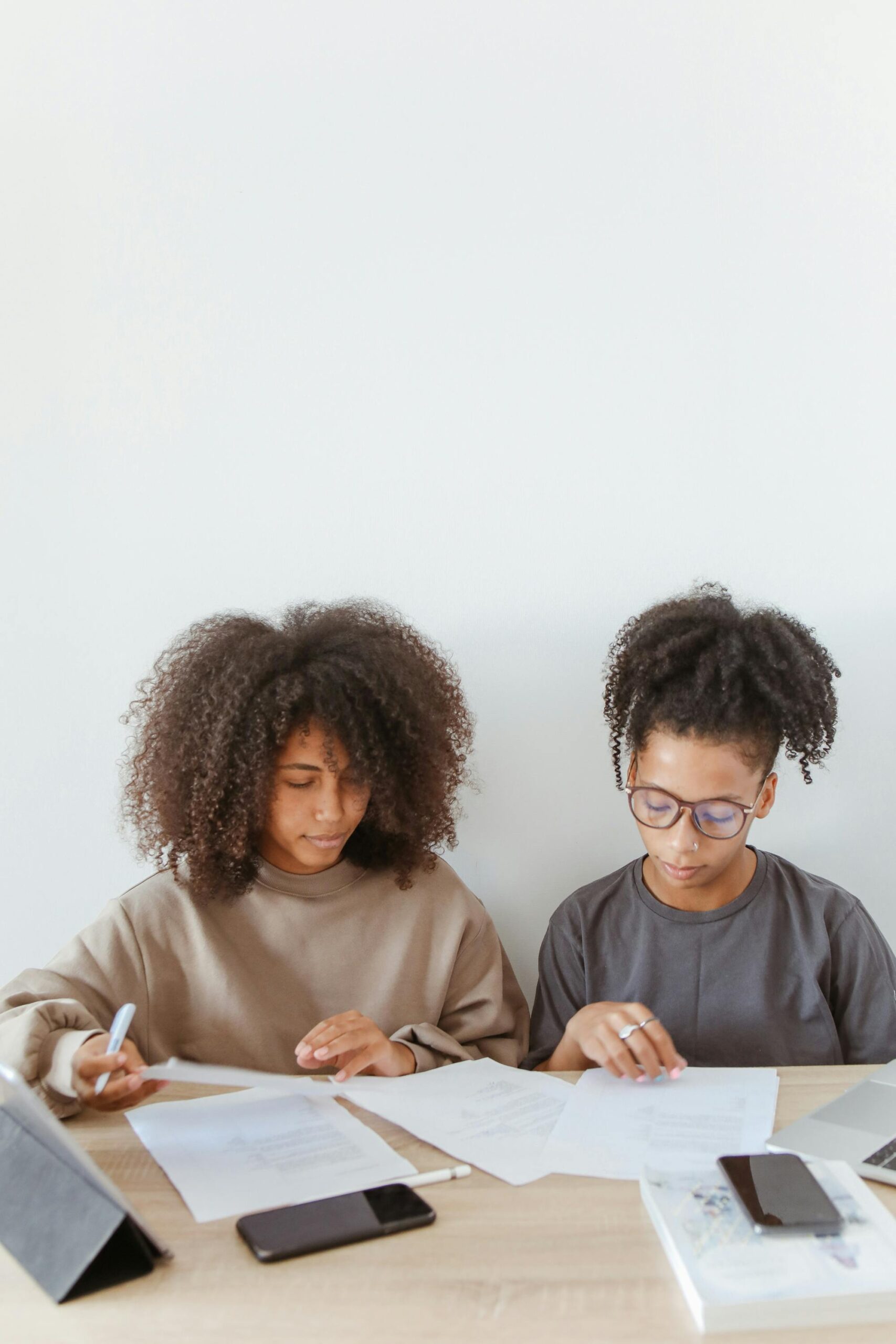 Two young women with curly hair reading papers at a table indoors.