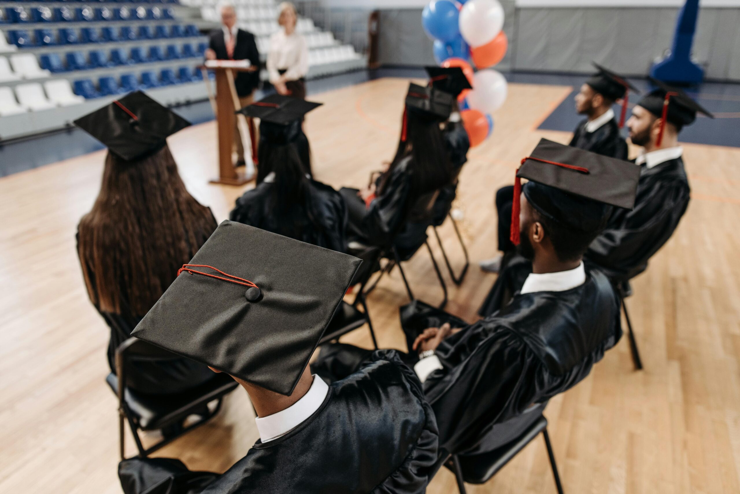Group of students in caps and gowns attending a graduation ceremony indoors.